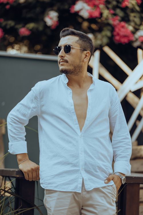 Free Fashionable man wearing sunglasses and white shirt poses outdoors with floral background. Stock Photo