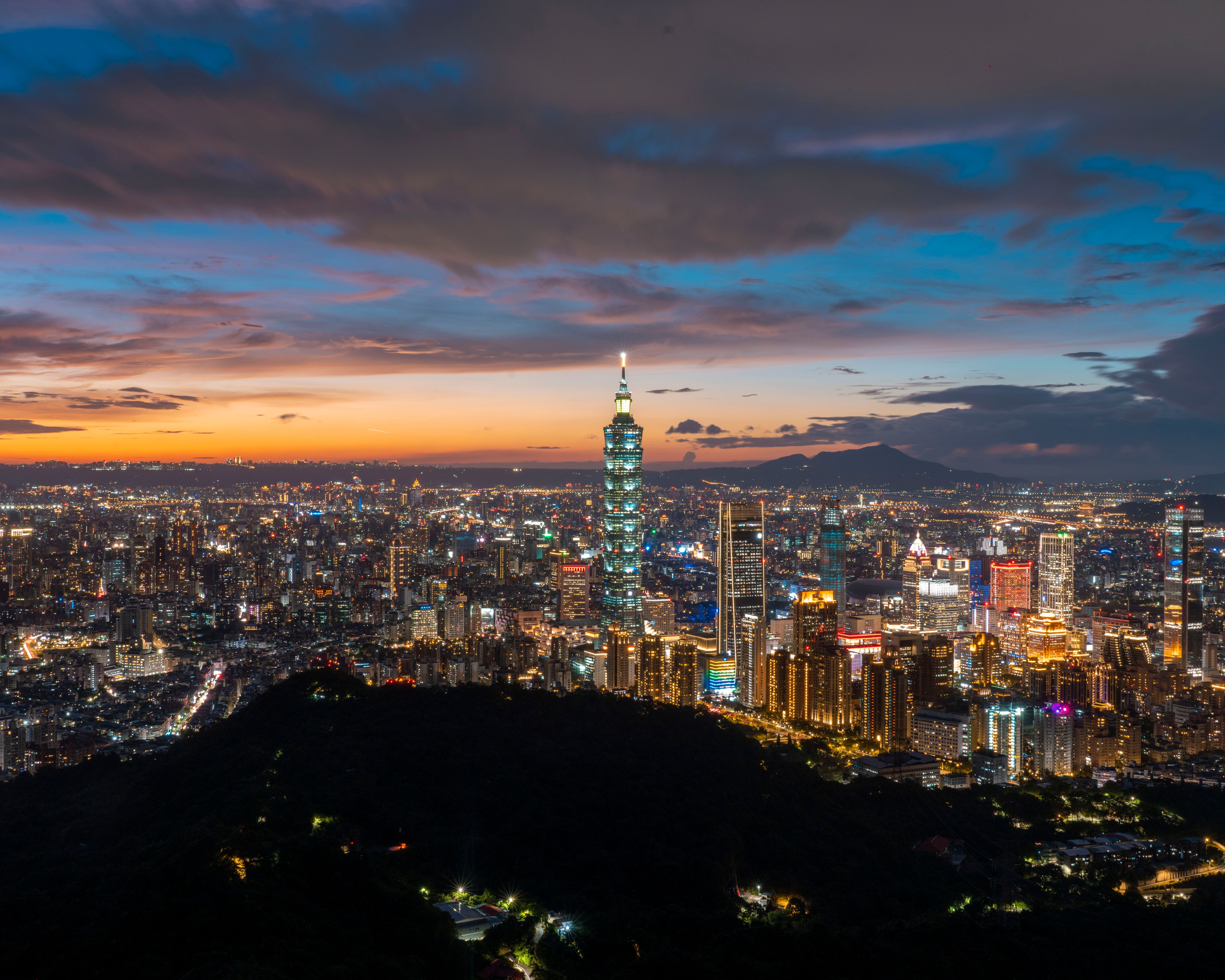 A stunning sunset view of Taipei City featuring the iconic Taipei 101 surrounded by a glowing urban landscape.