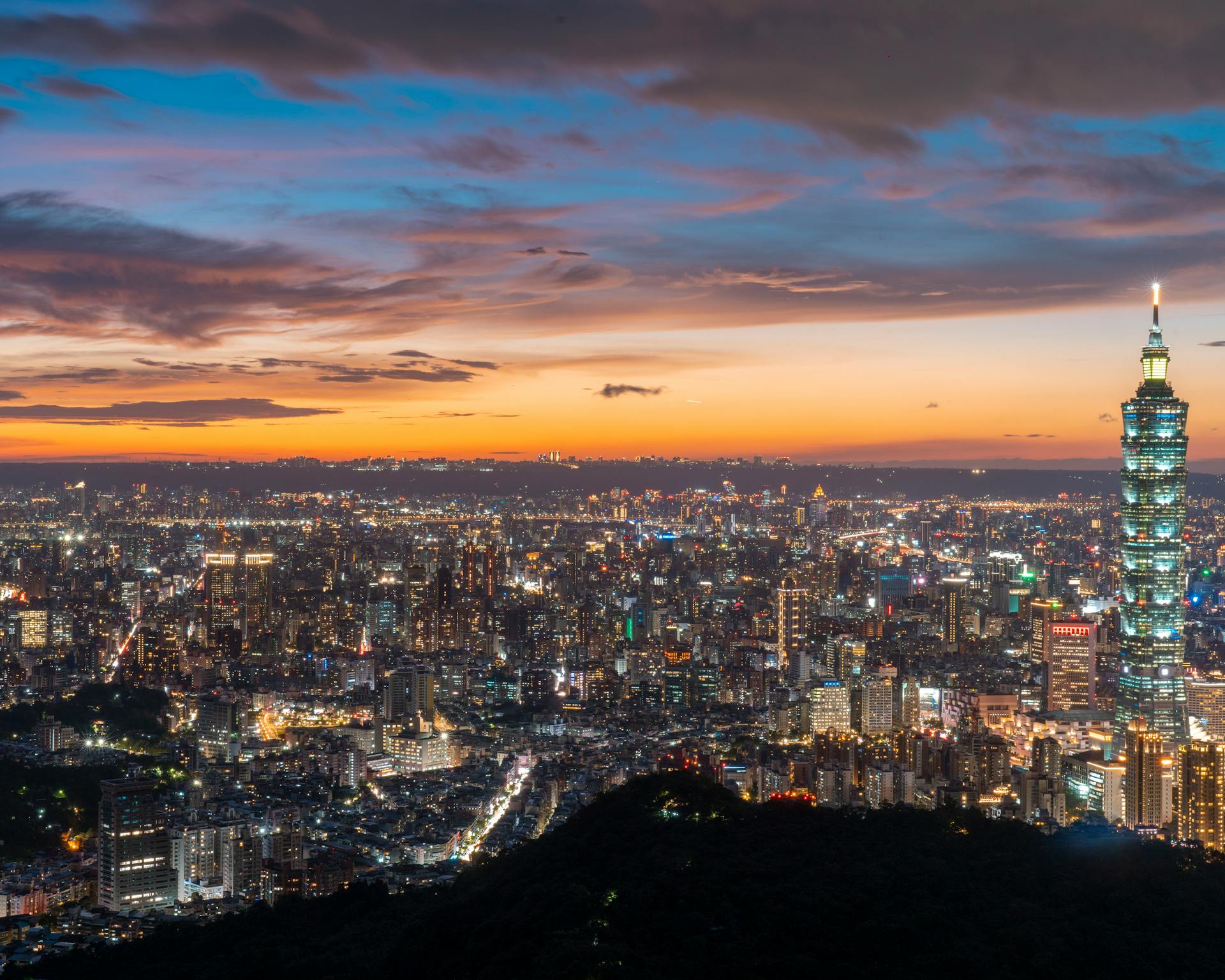 Taipei cityscape at dusk featuring the iconic Taipei 101 skyscraper illuminated against a vibrant sky.