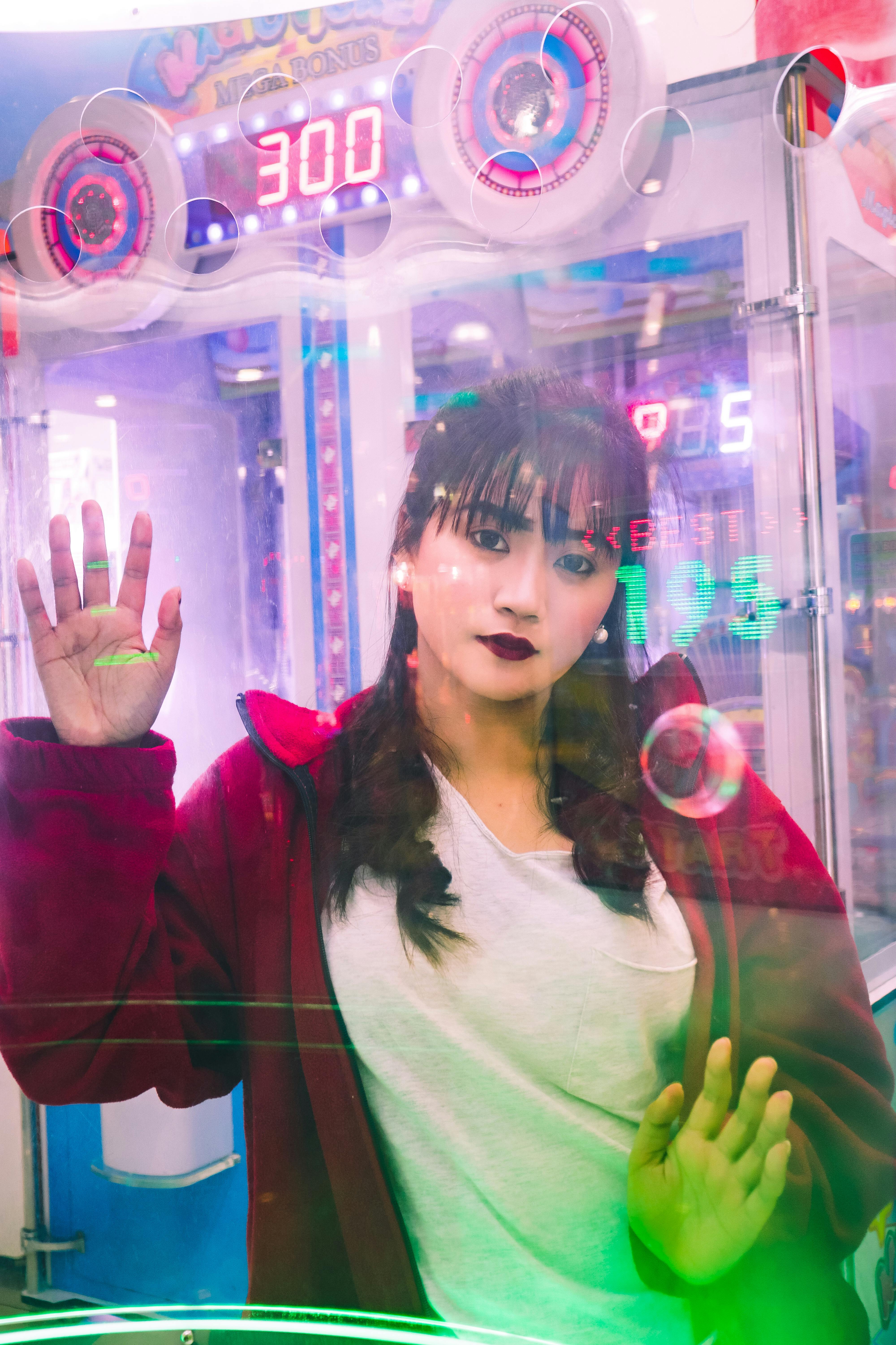 Young woman in a red jacket at an arcade game surrounded by neon lights.