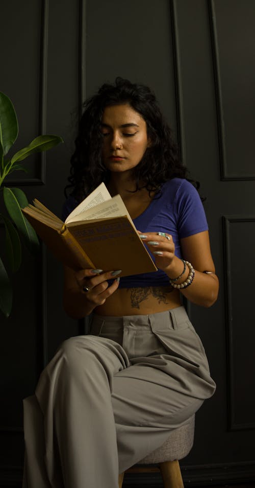Young Woman Sitting on a Chair by the Wall and Reading a Book 