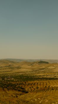 Expansive rural landscape with rolling hills and fields under clear sky.