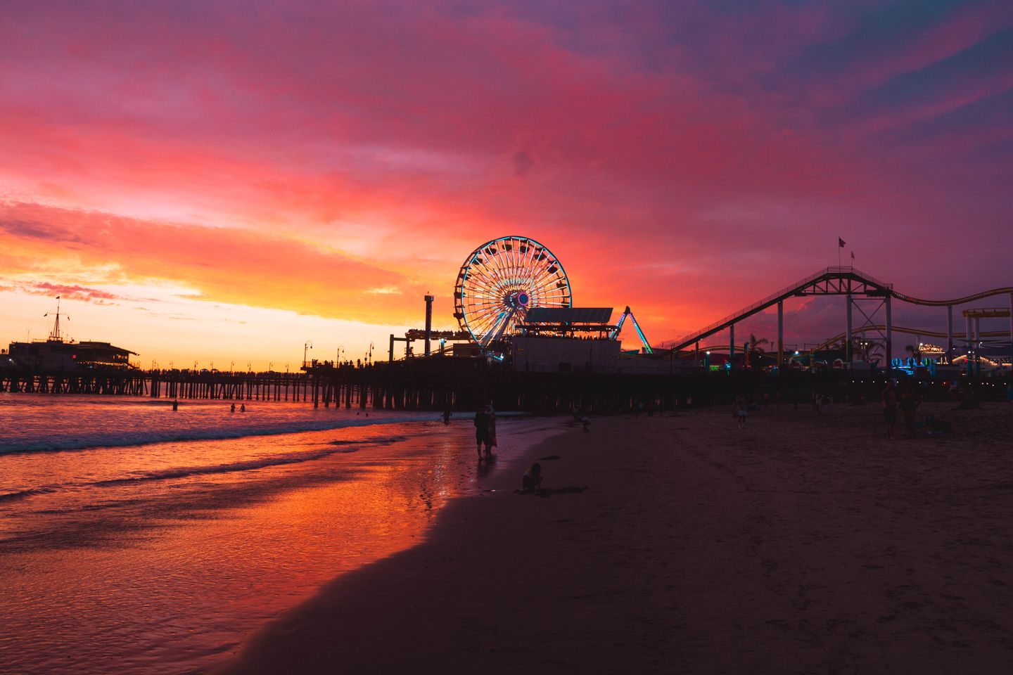 Santa Monica Pier at sunset with vibrant pink and orange sky, illuminated Ferris wheel, and beach