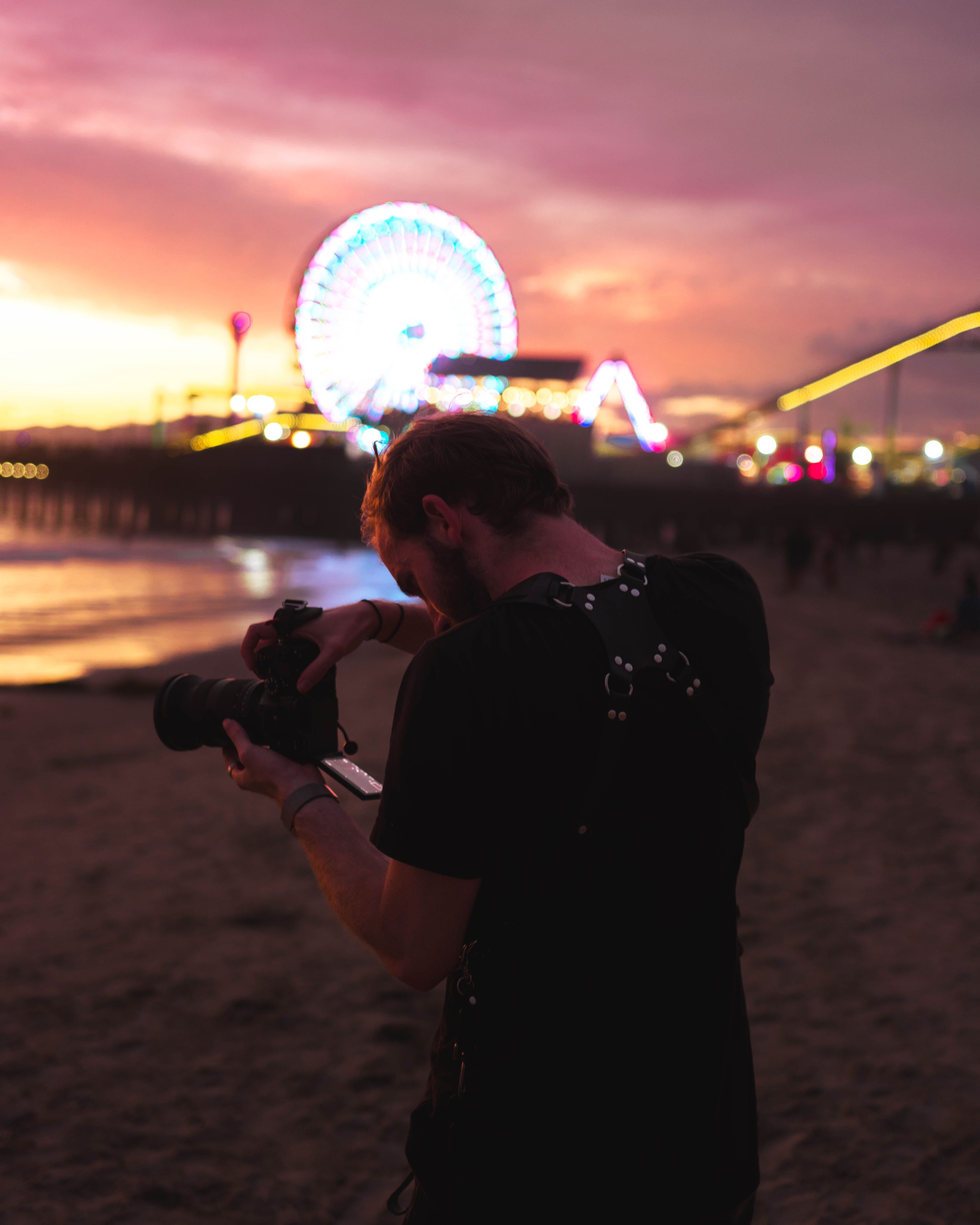 A photographer takes pictures of a stunning beach funfair at sunset, capturing vibrant colors and atmosphere.