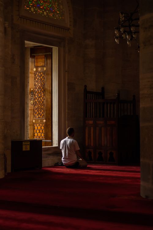 Free A man in prayer inside an Istanbul mosque, showcasing a beautifully carved wooden door and red carpet. Stock Photo