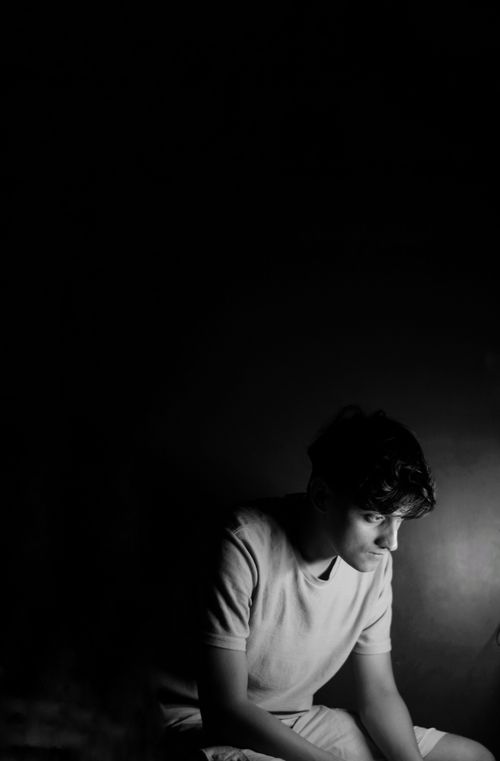 Free Dramatic black and white portrait of a young man with focused lighting creating a shadow effect. Stock Photo