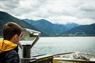 A teenage boy uses binoculars to observe a mountain lake view, capturing nature's beauty.