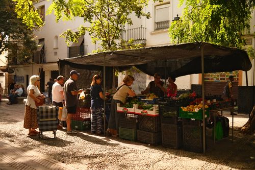 Free A bustling street market with people buying fresh produce in a sunny urban setting. Stock Photo