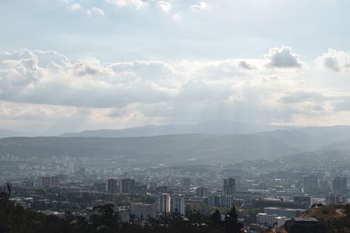 Free A panoramic view of a cityscape with hills, sunlight, and clouds creating an ethereal atmosphere. Stock Photo