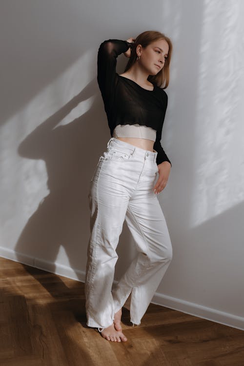 Young Blonde Woman in White Jeans and Black Long Sleeved Crop Top Leaning on a Wall