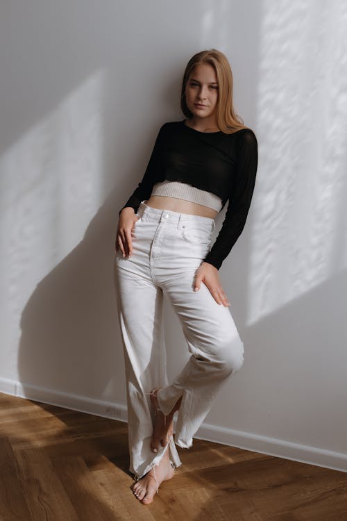 Young Woman in White Jeans and Black Crop Top Standing Barefoot by a Wall
