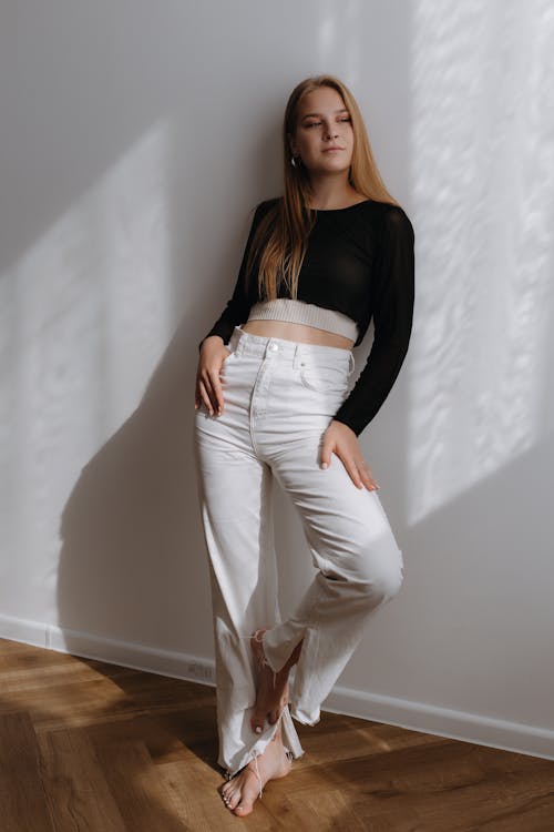 Blonde Woman in Black Crop Top and White Pants Posing by a Wall