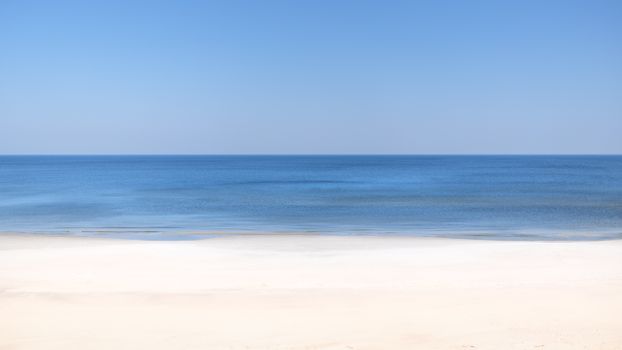 A tranquil beach scene with clear blue skies and calm ocean waves.