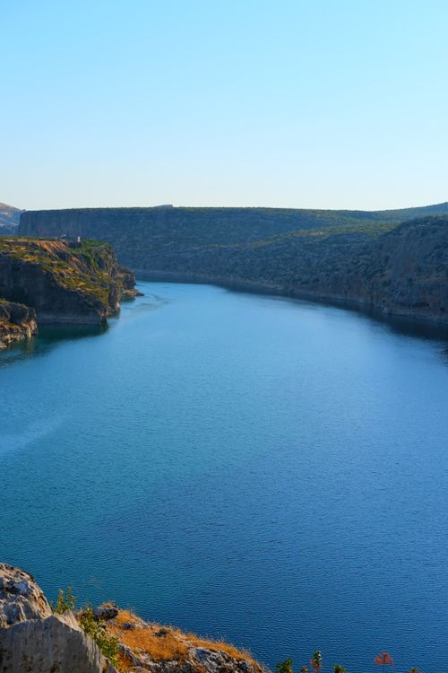 Free A serene view of a lake surrounded by rocky hills under a clear blue sky, perfect for nature and travel themes. Stock Photo