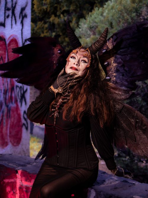 Free A woman in a devil costume with horns and wings poses creatively in an outdoor setting with graffiti. Stock Photo