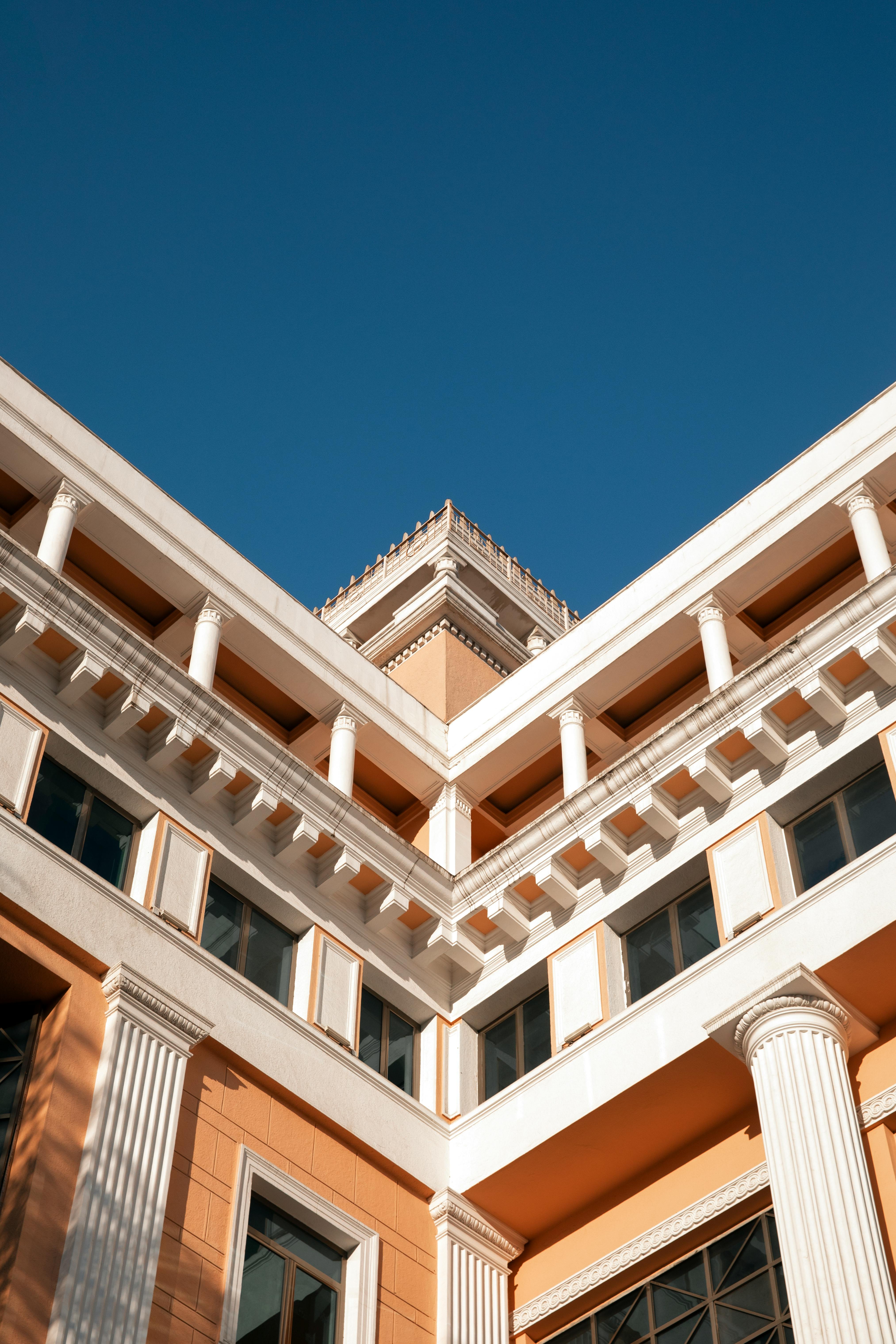 Free Elegant peach and white building facade with classical columns against a clear blue sky. Stock Photo