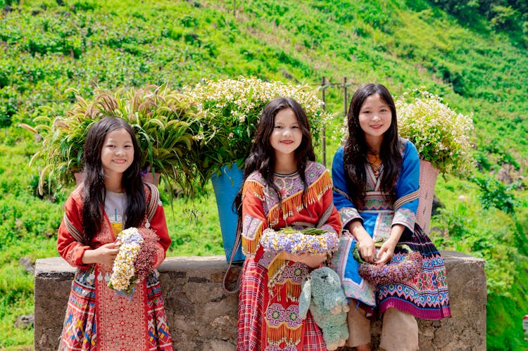 Smiling Girls In Traditional Clothing Sitting With Baskets Of Flowers