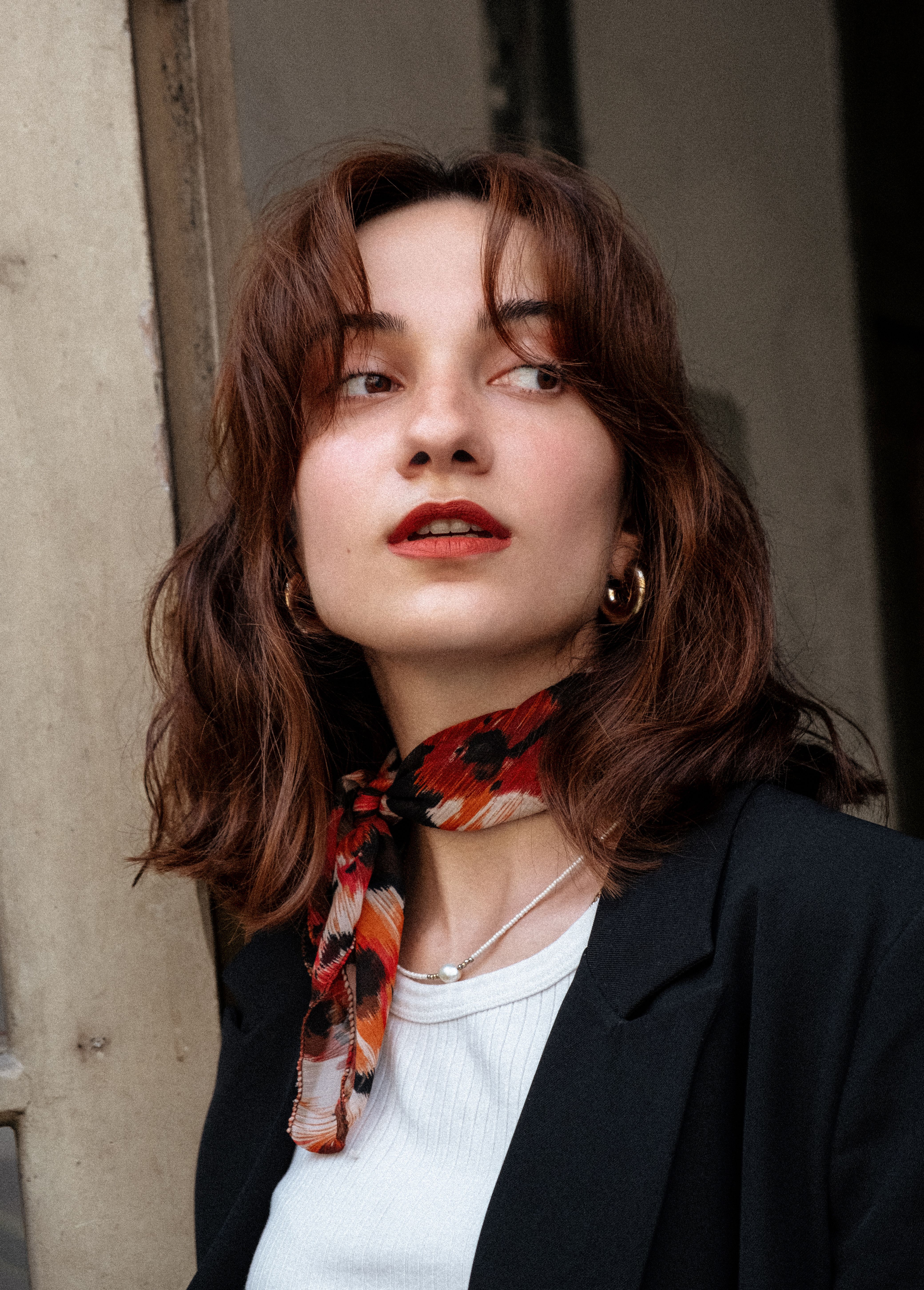 Portrait of a stylish woman with a scarf, elegant earrings, and red lipstick looking sideways.