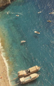 High angle view of boats moored on a turquoise beach with people relaxing on the sandy shore.