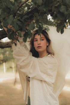 Elegant portrait of a woman in a white shirt standing under a tree on a sunny day.