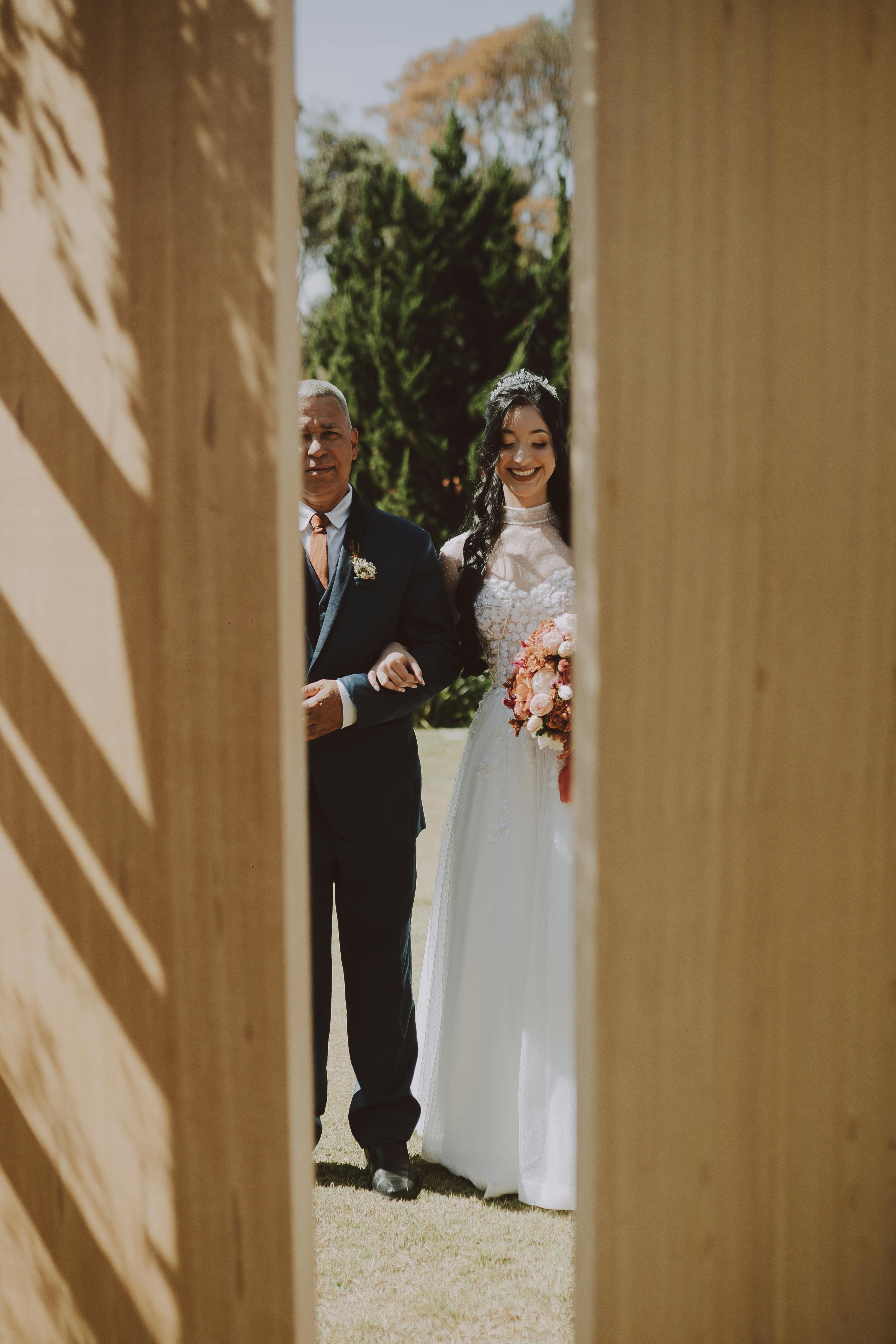 A bride enters with her companion through an outdoor setup framed by wooden structures.