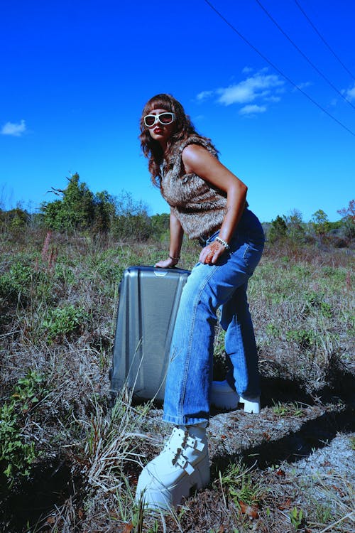 Woman in Vest and Sunglasses Posing with Suitcase