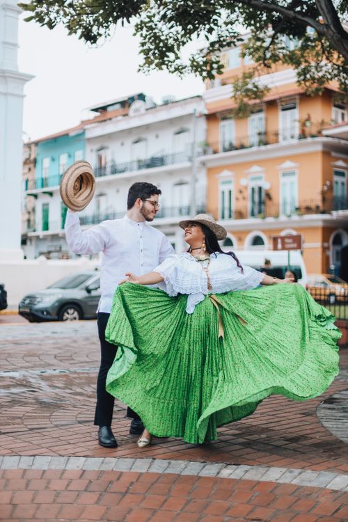 Free A joyous couple dancing in vibrant traditional clothing in a picturesque urban square. Stock Photo