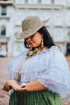 A woman in traditional Hispanic clothing with a hat, posing outdoors. Urban backdrop enhances the cultural vibe.