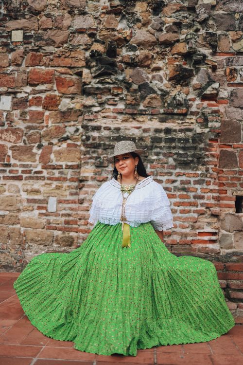 Free Woman in vibrant green skirt poses against a rustic stone wall, showcasing traditional attire. Stock Photo