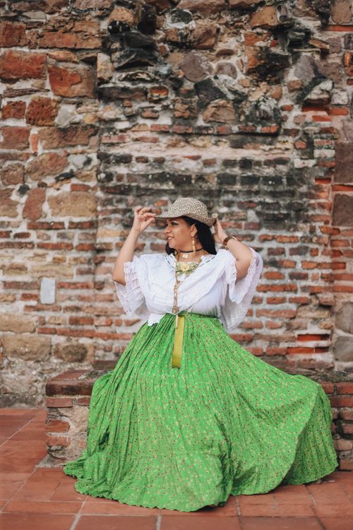 Free A woman in traditional attire with a hat poses against a rustic brick wall outdoors. Stock Photo