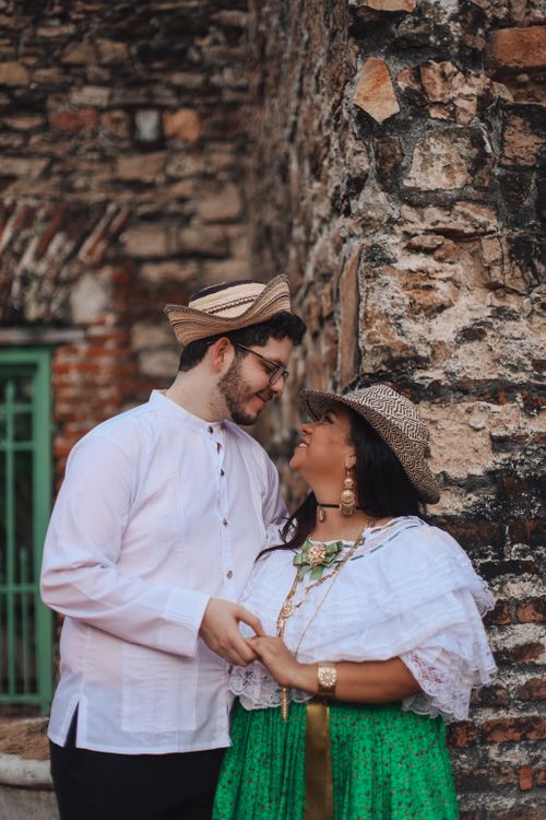 Free A joyful couple smiles warmly while dressed in traditional clothing, embracing against a stone wall. Stock Photo