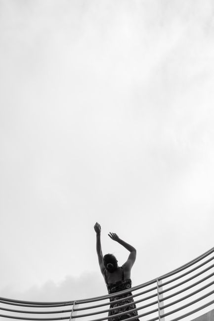 A woman poses on a balcony against a cloudy sky, creating a captivating silhouette.