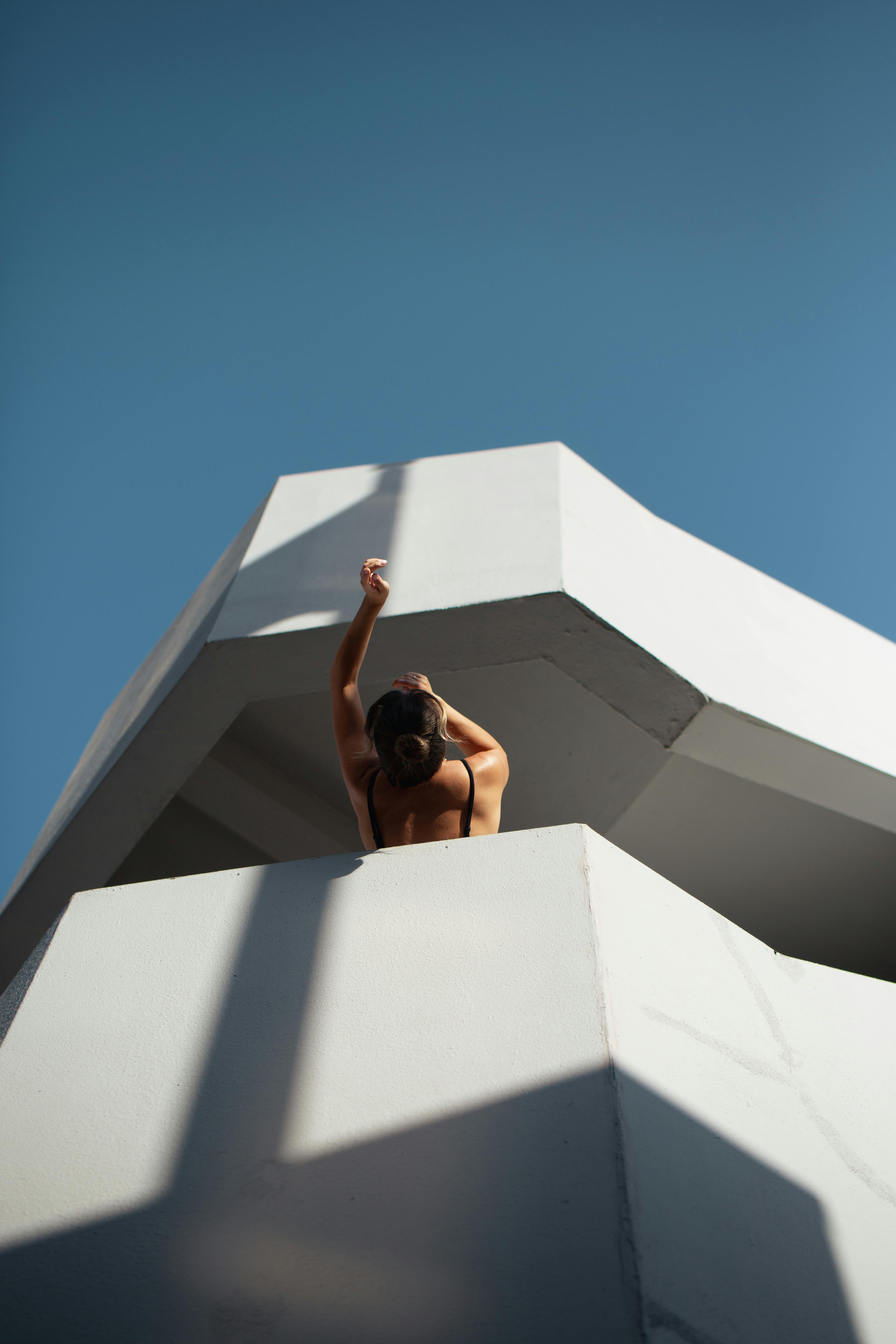 Woman leaning over a modern balcony under a clear blue sky.