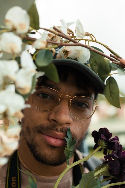 A man with glasses surrounded by flowers and greenery, smiling warmly.