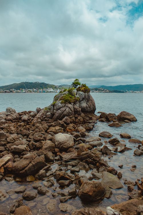 Free Scenic rocky seashore in Bombinhas, Brazil with cloudy skies and distant hills. Stock Photo