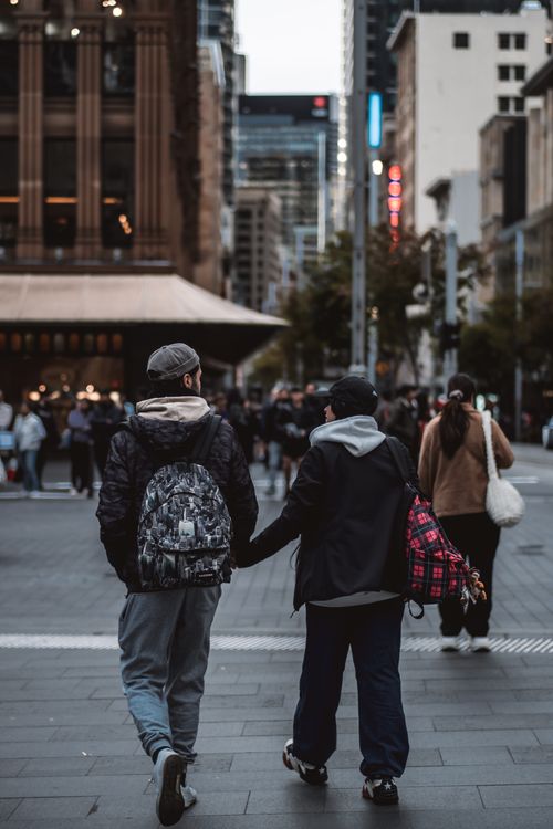 Free Two people walk hand in hand downtown, amidst the crowded city evening vibe. Stock Photo