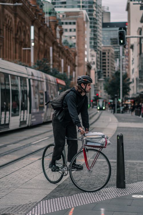 Free A cyclist stops at a crosswalk with a tram and city buildings in the background. Stock Photo