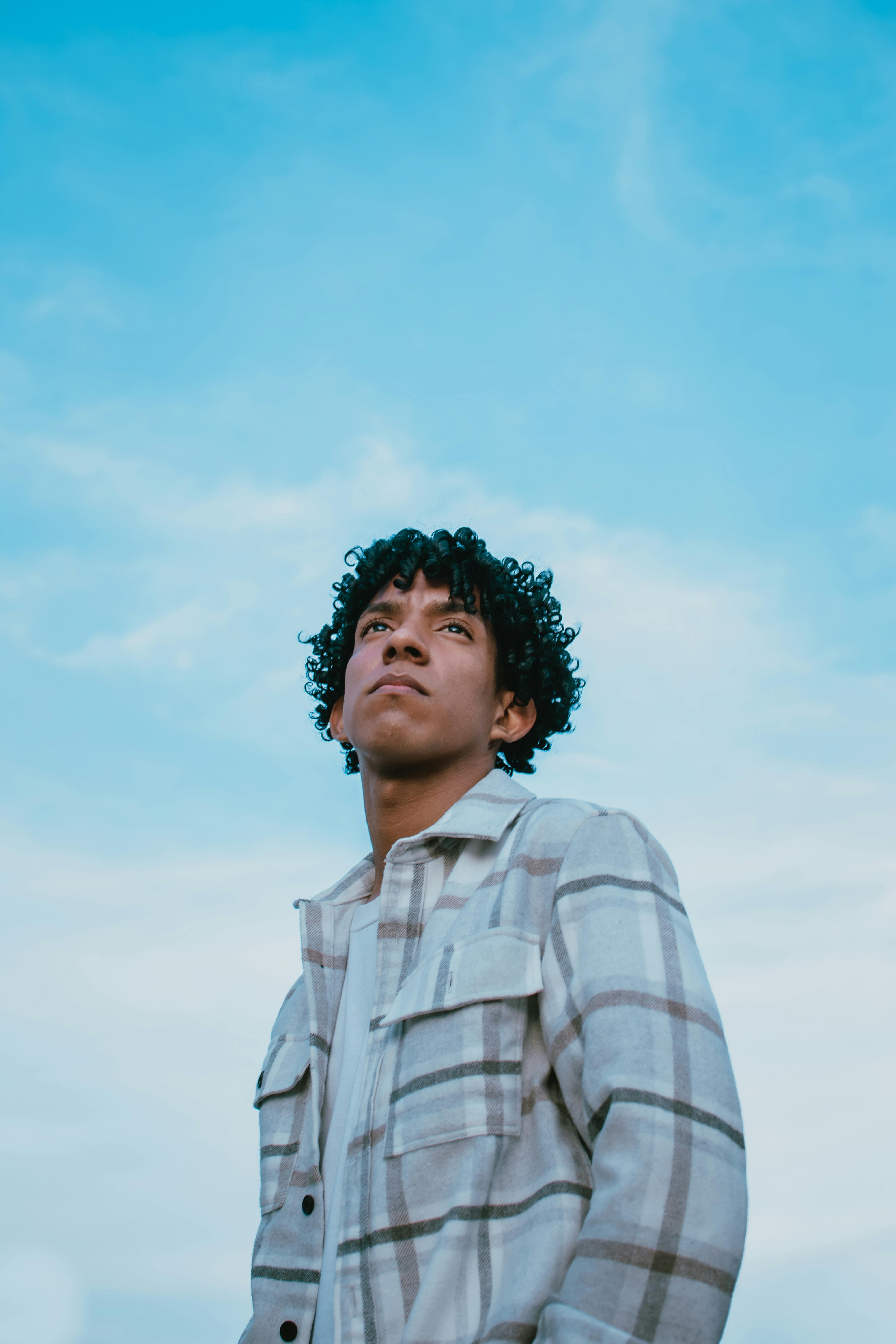A young man in a plaid jacket looking up against a blue sky. Captivating and stylish fashion portrait.