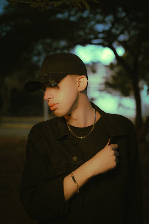 Young Man in a Black Denim Jacket and Baseball Cap in the Park