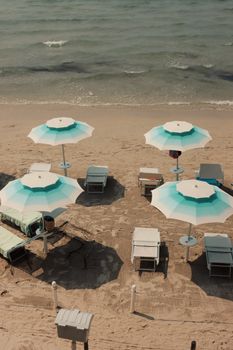 A tranquil beach scene in Alghero, Sardinia featuring umbrellas and sun loungers on a sandy shoreline.