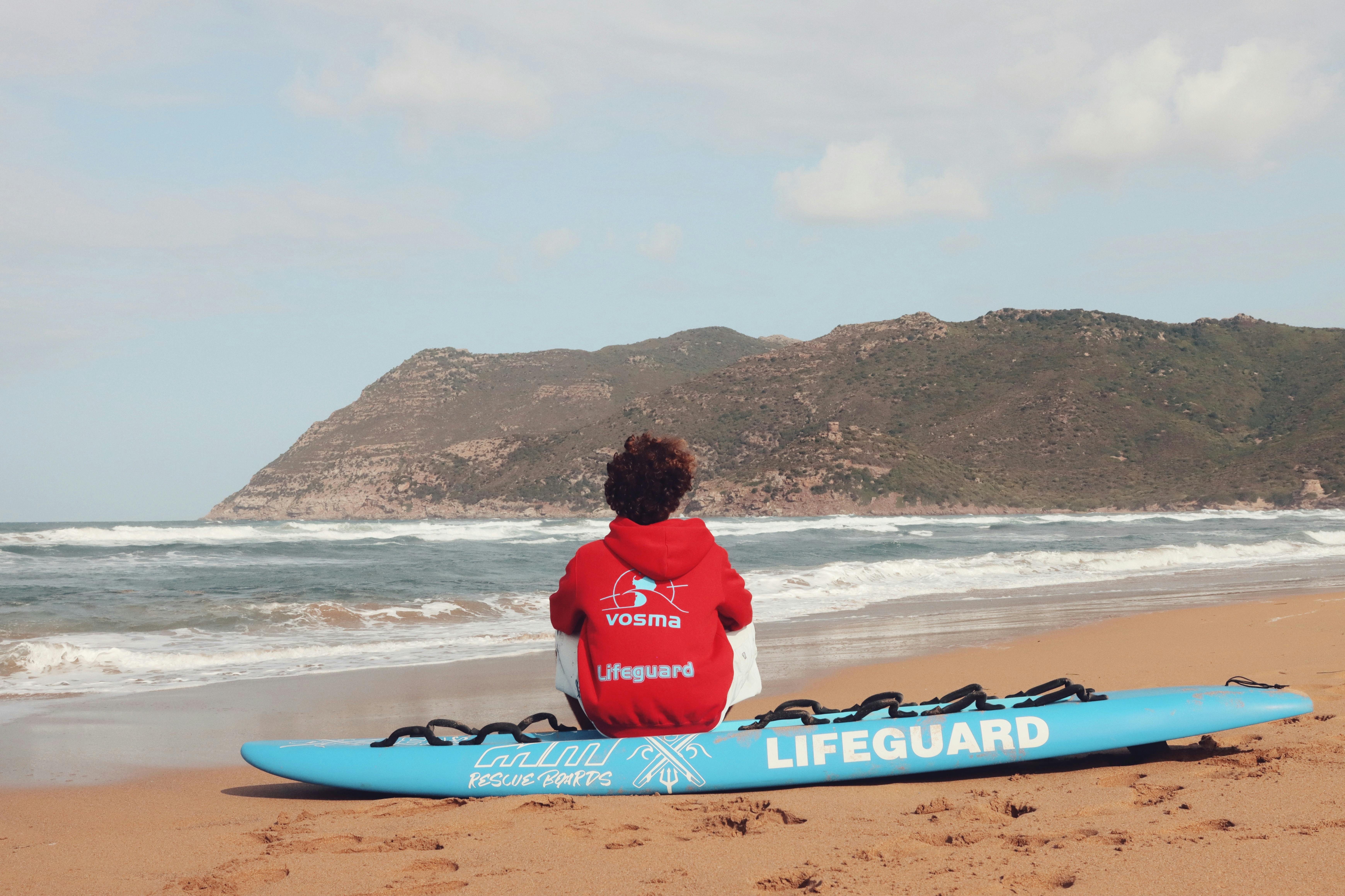 A lifeguard in a red hoodie sits on a beach in Alghero, Sardinia, Italy.