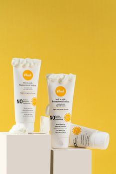 Close-up of sunscreen tubes displayed on white blocks against a yellow background, ideal for skincare promotions.