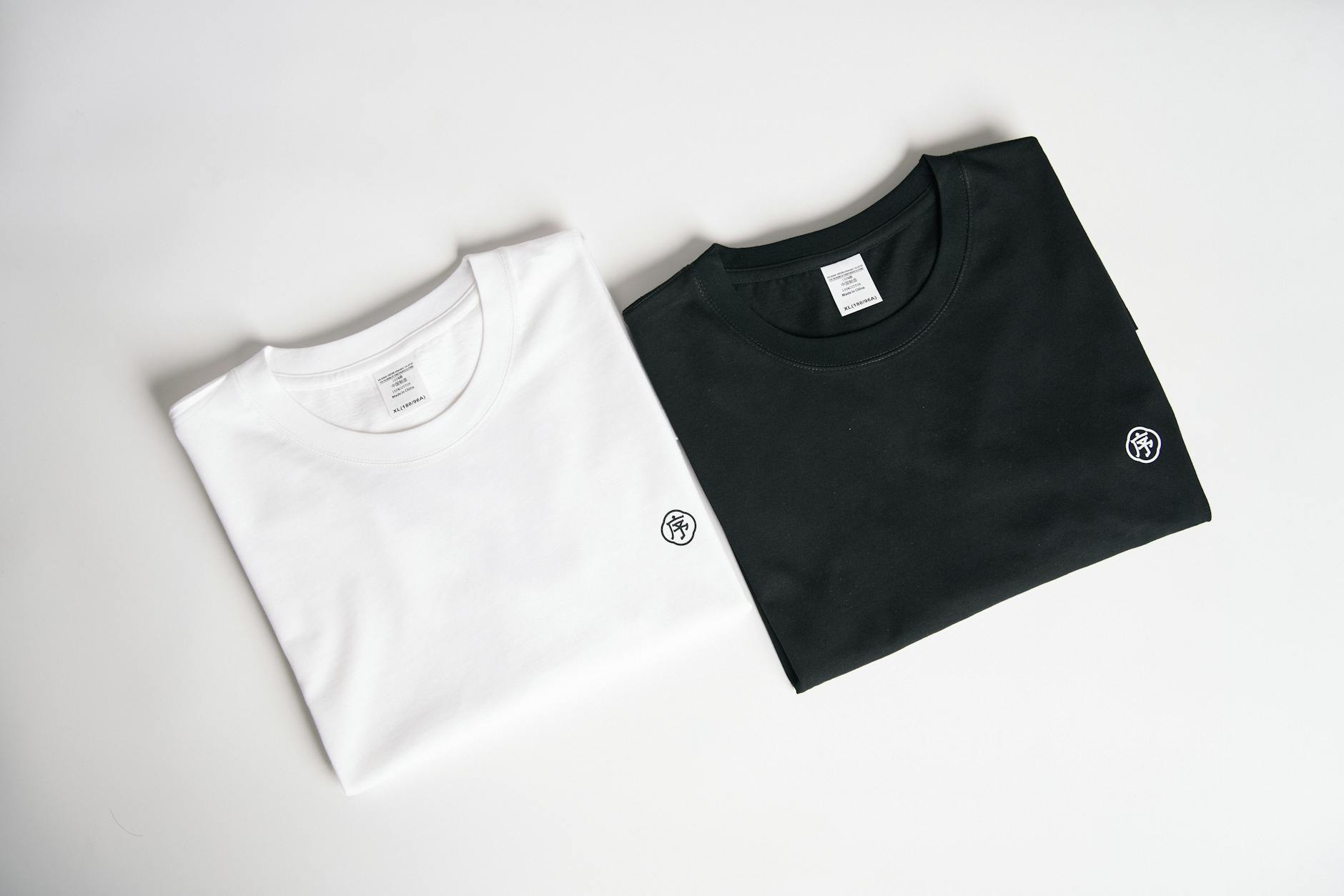 Two folded t-shirts, one black and one white, on a plain background in a minimalist style.