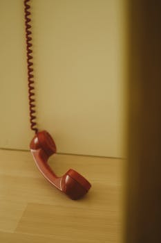 Close-up of a red vintage telephone handset resting on a wooden floor with a coiled wire.