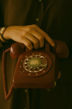 Close-up of a vintage rotary phone held by a woman's hands, evoking nostalgia and retro vibes.