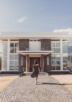A woman walks towards a modern residential house with a stone facade on a clear day.