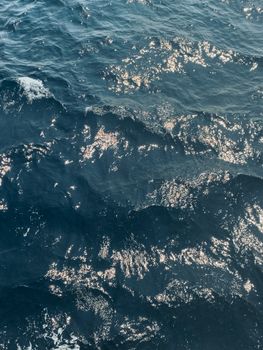 High angle view of blue ocean waves with shimmering sunlight reflections creating a wavy pattern.