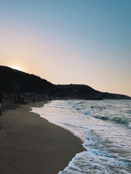 A tranquil beach scene at sunset with gentle waves and a hillside silhouette.