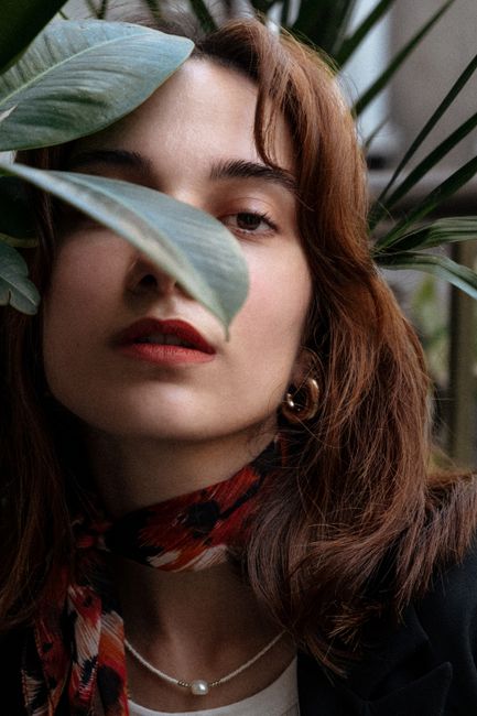 Stylish portrait of a woman partially obscured by leaves, conveying mystery and elegance.