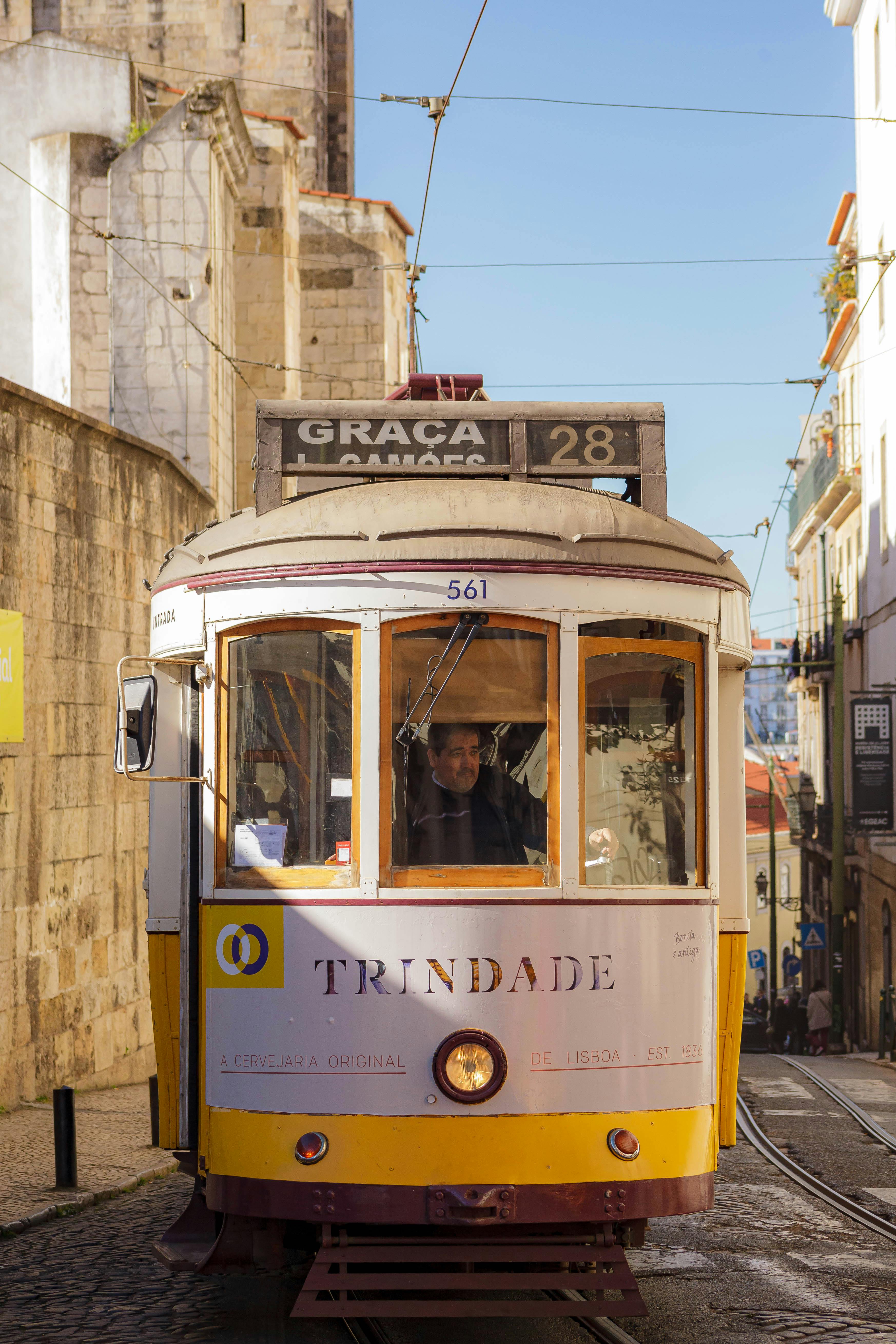 A historic tram in Lisbon, Portugal, travels through narrow city streets under a clear sky.